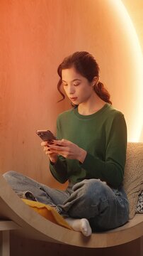 Focused Asian female freelancer texts on cellphone in home study, communication