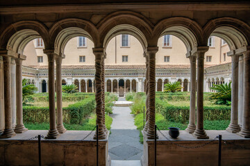 Fototapeta premium View through medieval cloister arcade and cosmatesque spiral columns into the inner garden at the Basilica of Saint Paul Outside the Walls in Rome Italy
