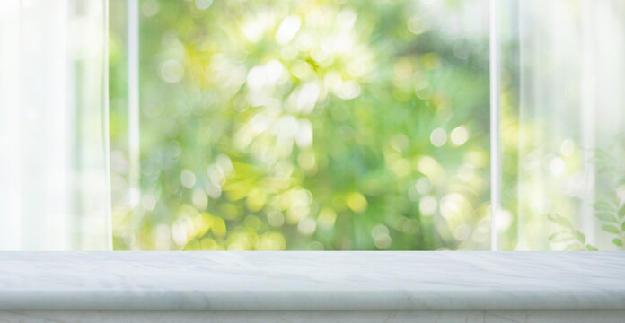 Selective focus.Bright marble countertop in the foreground, with blurred window glass view with green garden