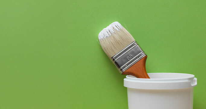 Paint Brush Resting Inside White Paint Bucket Container Against Green Background
