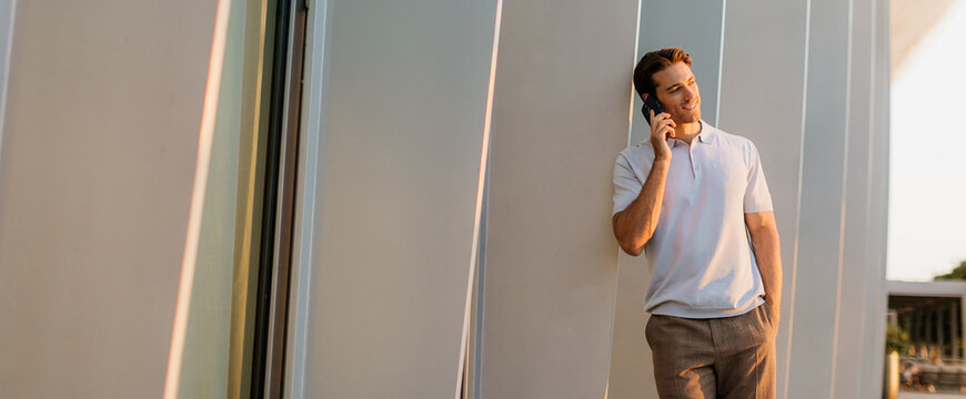Man leans against a wall while talking on the phone during golden hour