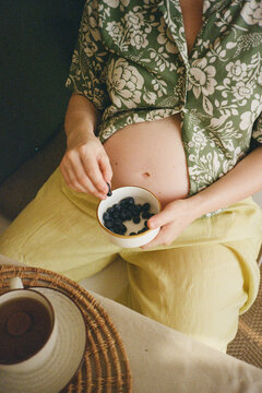 Pregnant woman resting a bowl of blueberries on her baby bump.