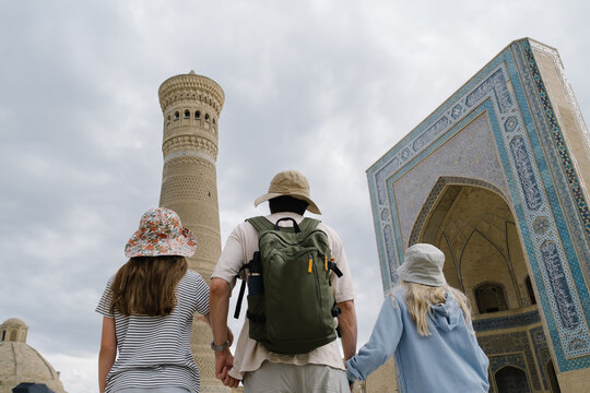 Family holding hands walking toward Kalyan Minaret in Bukhara.
