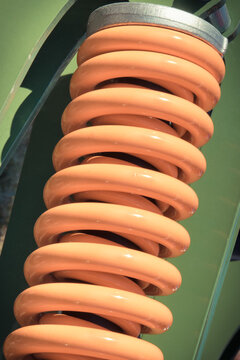 Steel orange spring as part of green heavy agricultural, industrial machine. Technology