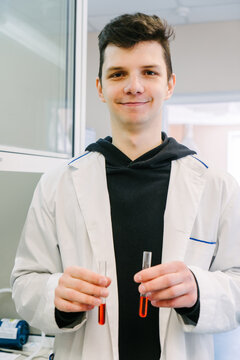 A chemist in a lab coat holds test tubes with liquid.