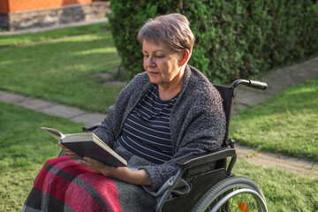 Fototapeta premium Elderly woman reading book in wheelchair outdoors, illustrating healthcare, rehabilitation, social inclusion, accessible living, independence, wellbeing, active aging, dignity, quality of life