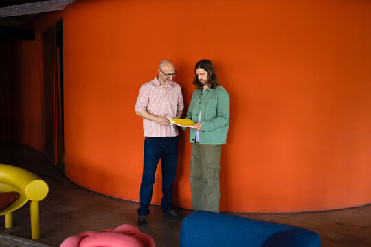 Two Men Reviewing Documents Against Orange Wall