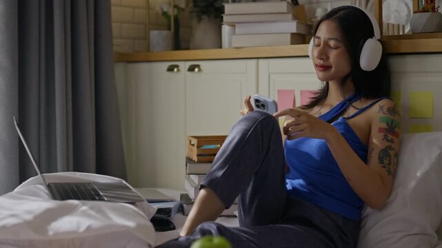 Happy young asian woman use smartphone and headphones Listening to music on streaming app and relaxing sitting on the bed at home.Enjoy,relaxation in morning and Time to relax concept