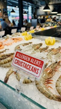 Fresh shrimp on ice with allergen alert sign crustaceans displayed at market for food allergy awareness and consumer safety