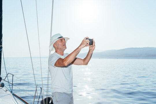 Mature man capturing vacation memories with smartphone on sailboat