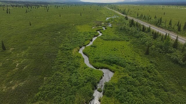 Aerial view of a winding creek snaking through the vast Alaskan tundra near a distant mountain range. July 11, 2025. 