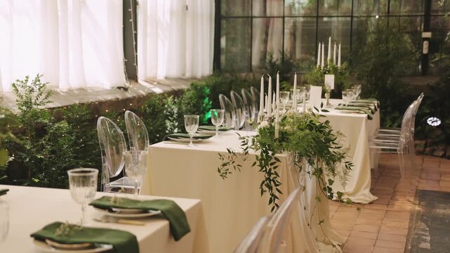 Wedding sweetheart table decorated with greenery, candles, glassware and green napkins for newlyweds.