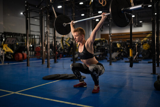 Strong sportswoman doing snatch exercise with barbell