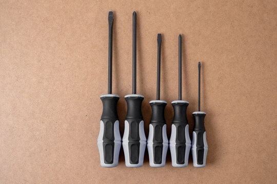 Five screwdrivers standing upright on hardboard background, top view