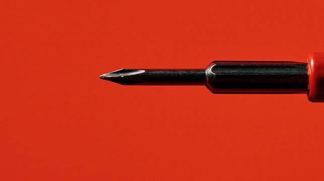 A sturdy metal screwdriver tip rests horizontally against a vibrant scarlet orange hue to emphasize the precision engineering required for manual hardware maintenance tasks during everyday