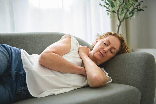 Happy 50s woman resting on comfortable sofa.