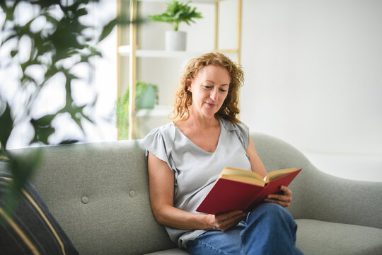 Pleasant middle aged woman involved in reading book.