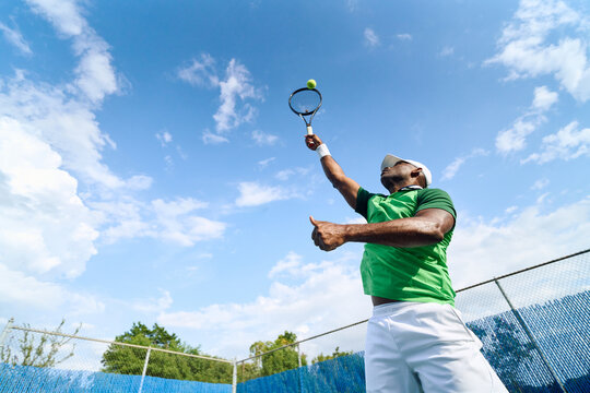 Tennis player serving a ball against a blue sky
