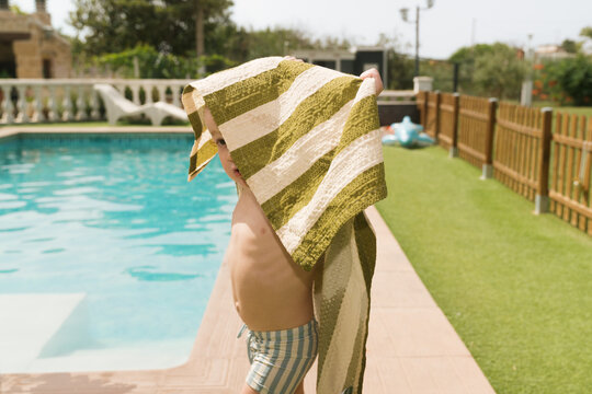 Child playing by the pool with a towel on a sunny day