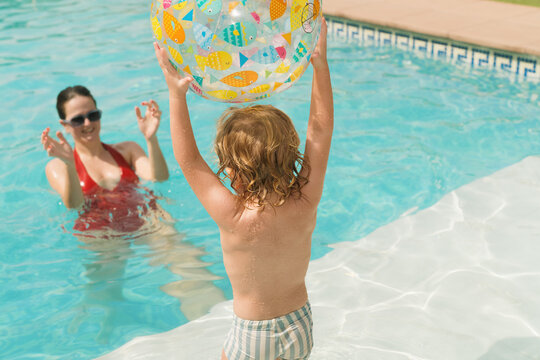 Child plays with beach ball in pool with adult nearby