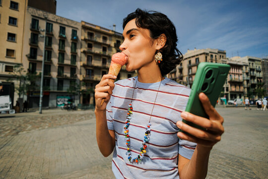 Woman enjoying ice cream and using smartphone in city