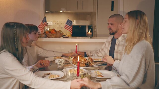 Family praying together and holding hands before their festive dinner on thanksgiving or christmas. Parents with their son and daughter are celebrating a holiday at home around the table