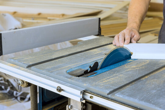 Carpenter operates table saw to cut piece of wood in workshop tools materials are visible around.