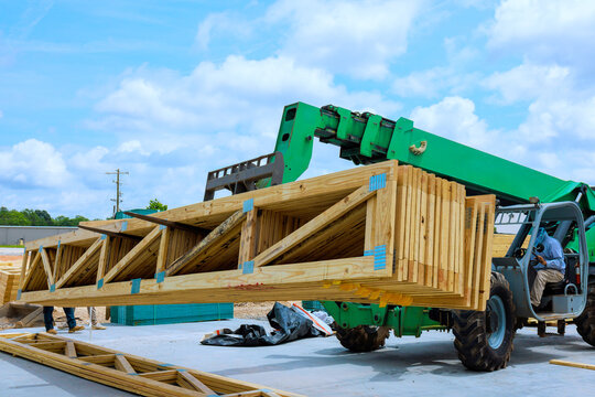 Worker operates telehandler lift to transport wooden trusses beams at construction site