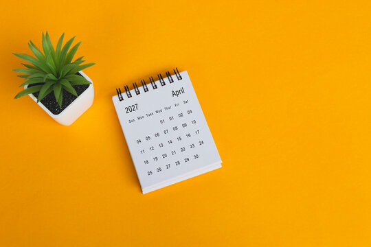 The April 2027 desk calendar with potted plant on yellow background.