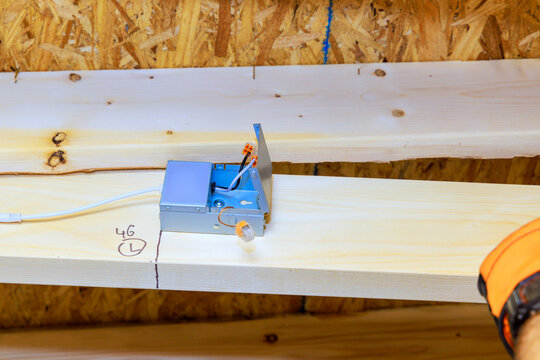 Contractor is installing an electrical box on wooden beam in building under construction