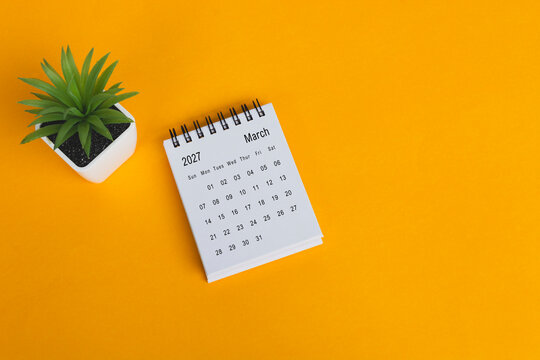The March 2027 desk calendar with potted plant on yellow background.