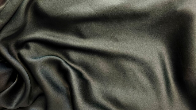 A close-up of dark green silk fabric with soft folds. A textile backdrop for clothing, upholstery, accessories, and decor.