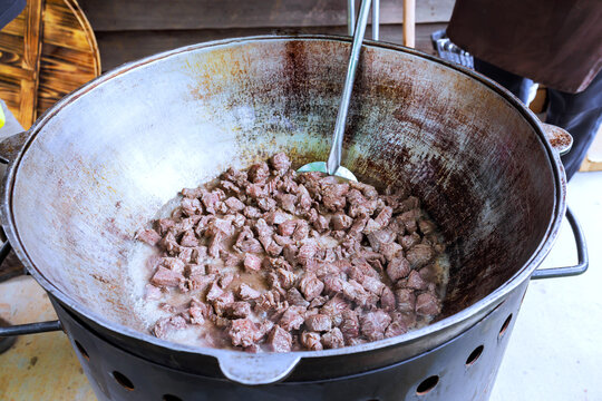 People cook meat in large pot at an outdoor gathering during chilly