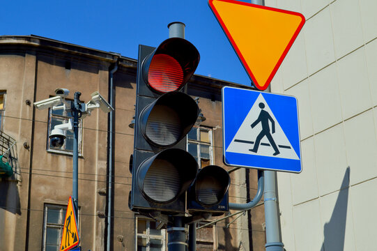Red traffic light with pedestrian crossing sign and yellow yield sign at urban city street intersection under clear blue sky