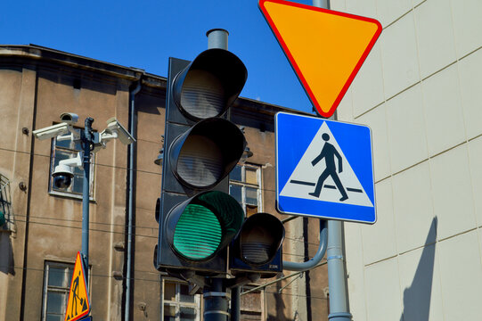 Bright green traffic light illuminated at a modern urban street intersection with pedestrian crossing sign and orange yield sign against clear blue sky