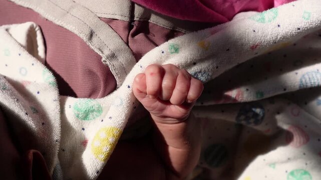 Close-up of a newborn baby's tiny hand wrapped in soft patterned blankets, capturing innocence and new life in a tender, natural moment for parenting and baby product marketing.