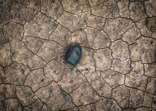 Aerial view of a single dark volcanic rock resting on parched, cracked earth with sparse green vegetation, Reykjanesbaer, Iceland.