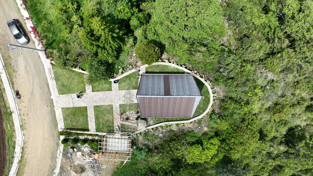 Aerial view of the Portezuelo area in Constanza, featuring a modern cabin with a metal roof, stone pathways, and lush green surroundings in the mountains of La Vega, Dominican Republic.