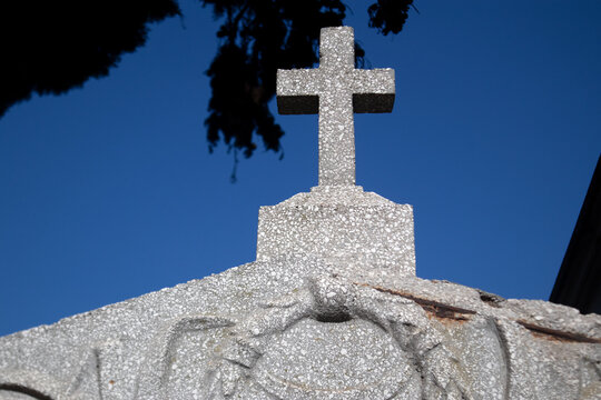 Dettaglio di una croce in pietra sopra una tomba monumentale in un cimitero monumentale storico con alberi e cielo blu sullo sfondo in una giornata di sole