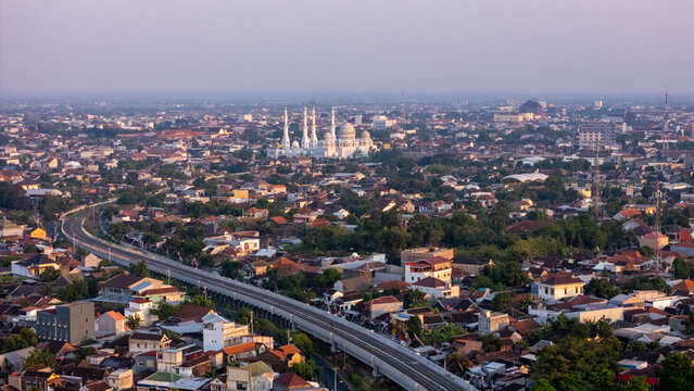 Aerial view of the Sheikh Zayed Grand Mosque surrounded by the dense urban landscape of Banjarsari, featuring rooftops, a railway viaduct, and greenery in Banjarsari, Central Java, Indonesia.