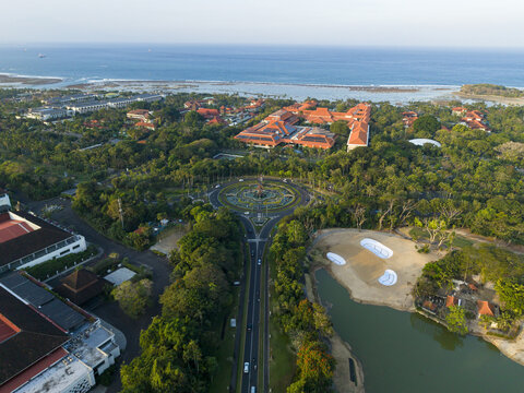 Aerial view of the lush green landscape and coastal road infrastructure surrounding the Nusa Dua area with tropical trees and resort buildings in Kecamatan Kuta Selatan, Bali, Indonesia.