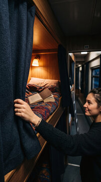 Young woman opening curtain to cozy sleeping bunk on night train journey