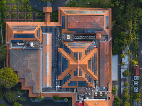 Aerial view of the Nusa Dua Resort Area Road building with solar panel arrays on its terracotta tiled roof, surrounded by lush greenery in Kecamatan Kuta Selatan, Bali, Indonesia.