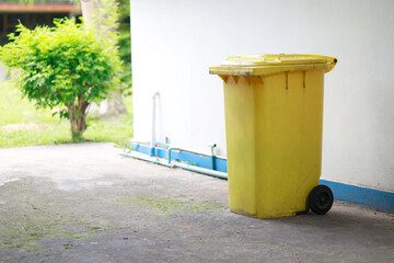 Fototapeta premium Large yellow wheeled garbage bin with lid placed outdoors beside a building, waste disposal, recycling, sanitation and environmental management