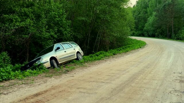 Car crash, wreck. The car went off the road as a result of an accident. The car is hanging off side of dirt road through forest as a result of an accident.