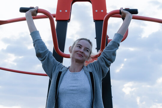 Woman doing lat pulldown exercise on outdoor fitness machine street gym