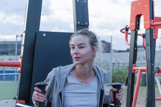 Blonde woman gripping handles on outdoor chest press fitness machine