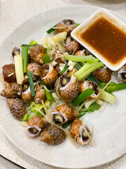 Steamed spotted babylon snails with lemongrass, ginger, scallions and dipping sauce served on white plate © Quyen