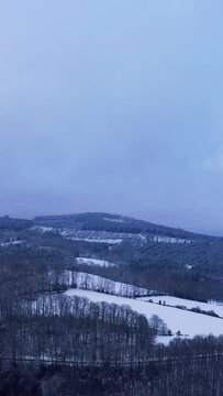 Vertical 9:16 aerial video of the Foret du Morvan at Haut Folin in Burgundy, France, showing rolling hills, dense forest, and open fields covered in fresh snow.