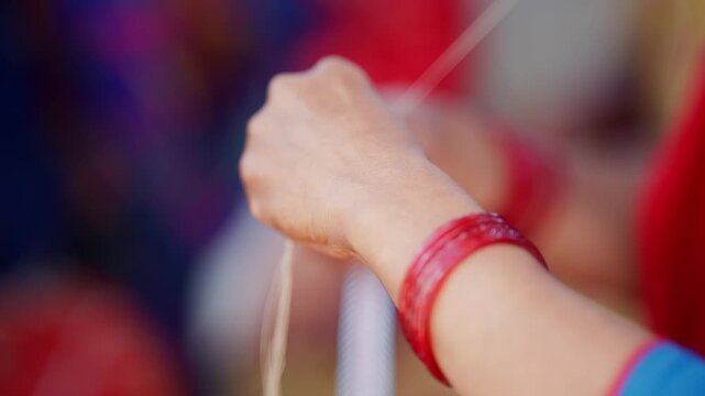 Close up of woman's hands with red bangles pulling white bead thread strands while weaving traditional pote necklace in rural Nepal